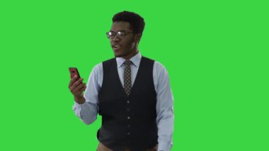 Gülümseyen Afrikalı Amerikalı işadamı elinde cep telefonuyla görüntülü arama yapıyor. Yeşil Ekran, Krom Anahtar 'da yürürken..