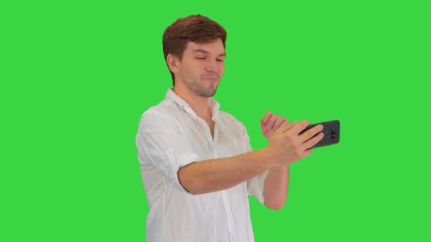 Młody mężczyzna w luźnej białej koszuli robi sobie selfie telefonem na zielonym ekranie, Chroma Key. — Wideo stockowe