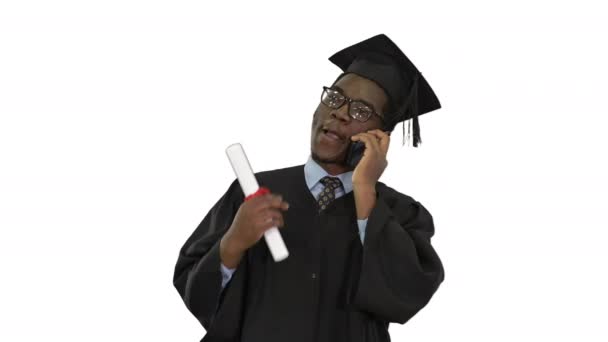 Gülümseyen Afro-Amerikan erkek öğrenci. Mezuniyet cübbesi içinde telefonda konuşuyor. Beyaz arka planda mutlu haberleri paylaşıyor.. — Stok video