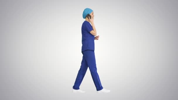 Serious female doctor talking on the phone while walking on gradient background. — Stock Video