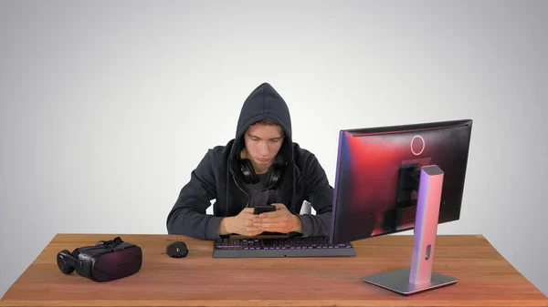 Hacker com capuz usando laptop e smartphone no fundo gradiente — Fotografia de Stock