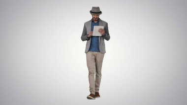 Şapkalı, yürüyen ve tablet kullanan yakışıklı, gülümseyen bir Arap.