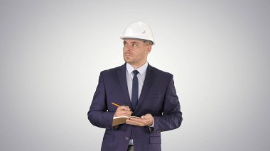 Takım elbiseli mühendis, kask takıyor ve not defterine notlar yazıyor.