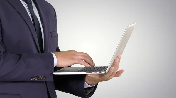 Empresário de pé e usando laptop no fundo gradiente. — Fotografia de Stock