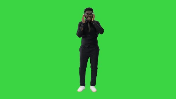 Afroamerikanischer Mann hält Kopfhörer mit beiden Händen und groovt zur Musik, während er lächelnd auf einem Green Screen in die Kamera blickt, Chroma Key. — Stockvideo