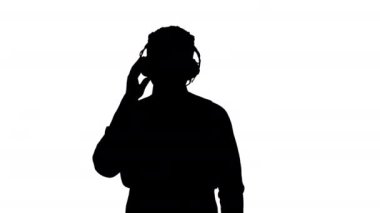 Siluet gülümseyen Afro-Amerikan kulaklıklı adam yürürken ve kameraya bakarken müzik dinliyor..