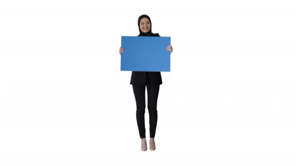 Mujer árabe sonriente en hijab sosteniendo un cartel azul en blanco y mirándolo sobre fondo blanco. — Vídeo de stock