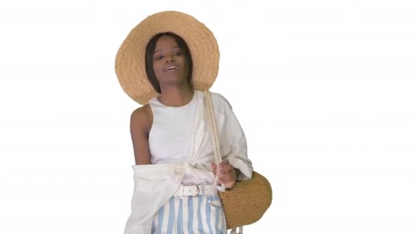 Ontspannen Afrikaans Amerikaans meisje lopen met een strohoed en een zak op witte achtergrond. — Stockvideo