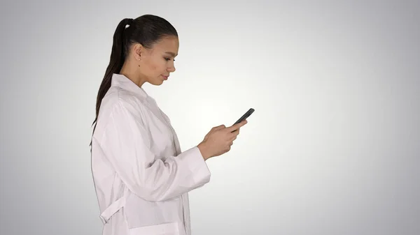 Alegre bonito jovem mulher médico digitando texto no telefone enquanto andar — Fotografia de Stock