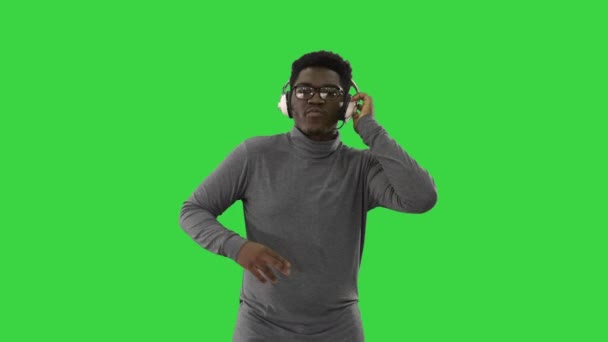 한 손으로는 헤드폰을 들고 녹색 화면 위에서 카메라를 들고 걷는 동안 음악에 심취하는 아프리카계 미국인 크로마 키 (Chroma Key). — 비디오