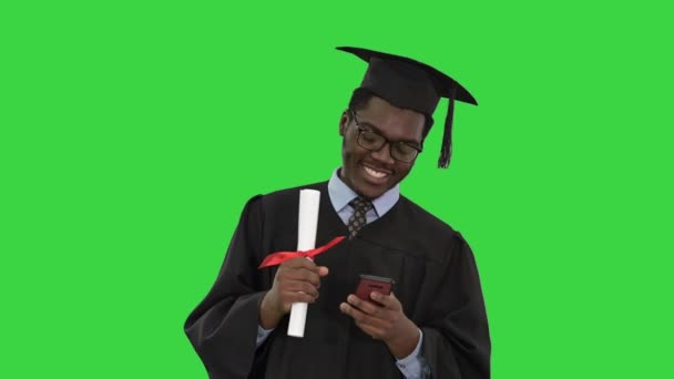 Souriant étudiant afro-américain de sexe masculin en robe de remise des diplômes avec des textos de diplôme au téléphone sur un écran vert, Chroma Key. — Video