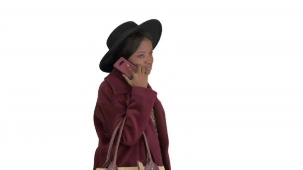 Beyaz arka planda yürürken siyah şapkalı Afrikalı Amerikalı moda kızı telefonda konuşuyor.. — Stok video
