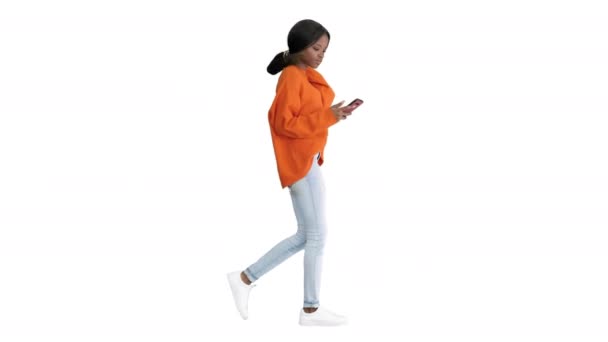 Donna sorridente digitando un messaggio di testo sul suo telefono mentre cammina su sfondo bianco. — Video Stock