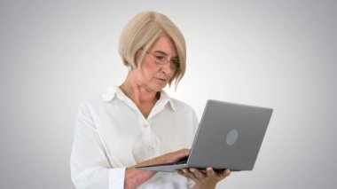 Gözlüklü, ciddi, olgun bir iş kadını, gradyan arka planda laptop kullanıyor..