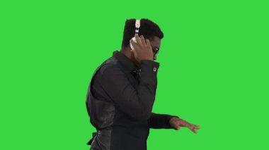 Genç Afro-Amerikalı adam kulaklıkla müzik dinliyor ve yeşil ekranda yürürken tıkırdıyor, Chroma Key.