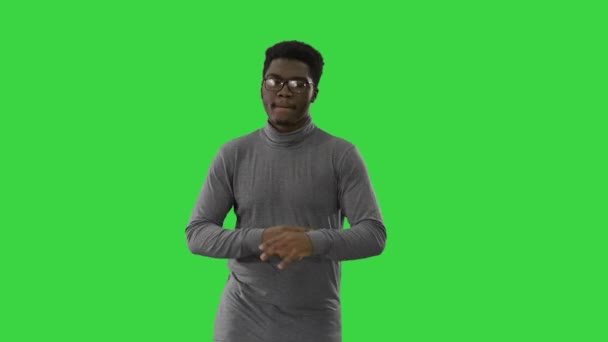 Jonge Afro-Amerikaanse man in grijze kleren en glazen groovend tijdens het lopen op een groen scherm, Chroma Key. — Stockvideo