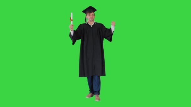 Männlicher Student in Abschlussrobe posiert mit seinem Diplom und macht lustige Gesichter auf einem Green Screen, Chroma Key. — Stockvideo