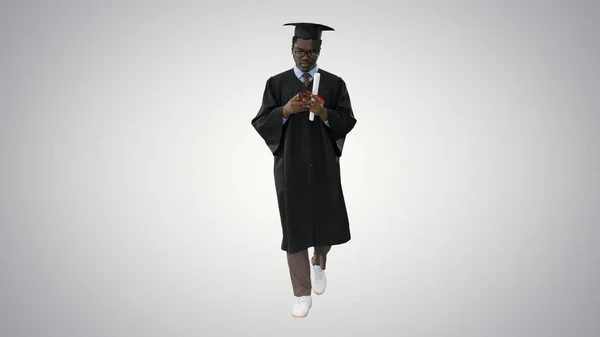 Afro americano maschio studente in laurea abito sms su il — Foto Stock