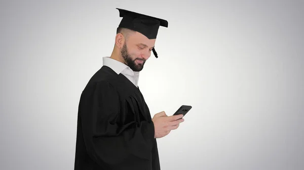 Graduado estudante andando e mensagem de texto no telefone em gra — Fotografia de Stock