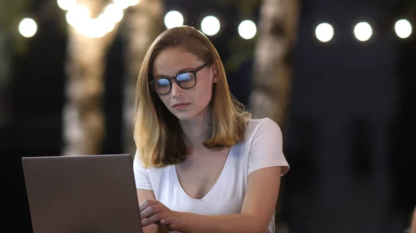 Jonge casual zakenvrouw in bril met laptop werken in de avond buiten. — Stockfoto