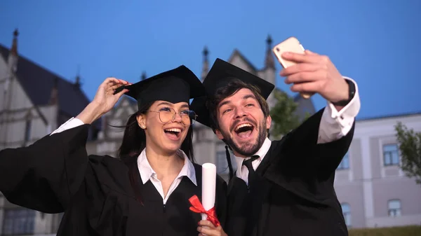 Mannelijke en vrouwelijke afgestudeerde studenten nemen een selfie met mobiele telefoon. Emotioneel koppel. — Stockfoto