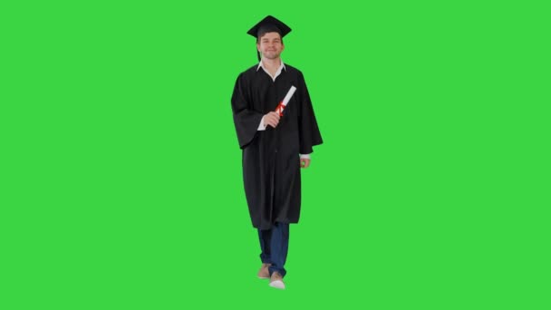 Mezuniyet cüppeli gülümseyen erkek öğrenci yeşil ekranda diplomasıyla yürüyor, Chroma Key.. — Stok video