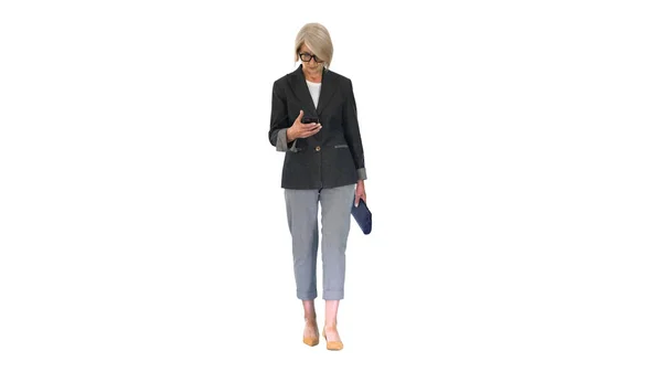 Mulher sênior inteligente usando smartphone enquanto caminha em branco — Fotografia de Stock