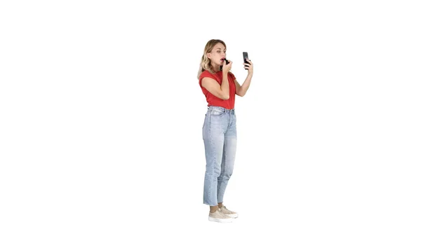 Frau benutzt Lippenstift und schaut in ihr Handy auf weißem Hintergrund — Stockfoto