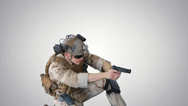 Soldado está atirando da pistola sentado em seu joelho em gradiente — Fotografia de Stock