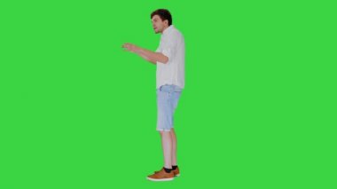 Heyecanlı genç adam günlük giysiler içinde bir hikaye anlatıyor ve yeşil ekranda işaret ediyor, Chroma Key.
