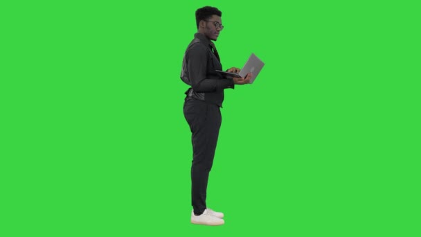 Афроамериканський бізнесмен, який друкує на ноутбуці і розмовляє з кимось з посмішкою, жестикулюючи на зеленому екрані, Chroma Key. — стокове відео
