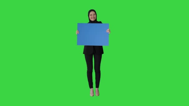 Посмішка арабської жінки в Хіджабі, яка тримає чистий синій плакат і дивиться на нього на зеленому екрані, Chroma Key. — стокове відео