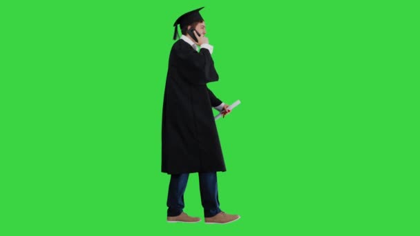穿着毕业礼服走路微笑的男生，并在绿色屏幕上打了个电话，铬键. — 图库视频影像