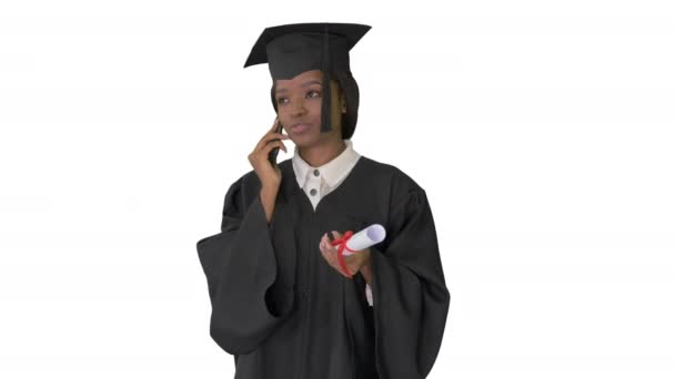 Afro-americana estudiante en bata de graduación hablando por teléfono sobre fondo blanco. — Vídeos de Stock