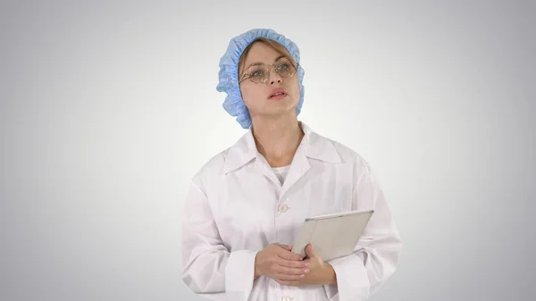 Женщина-врач держит планшет и ходит на градиентном фоне. — стоковое фото