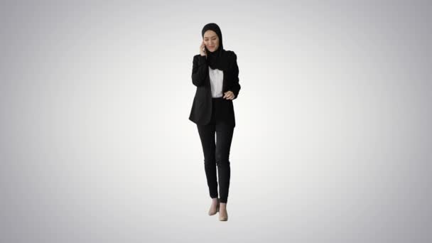 Atractiva mujer musulmana moderna caminando y hablando en el teléfono celular en el fondo gradiente. — Vídeos de Stock
