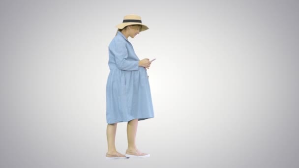 Mujer embarazada joven en sombrero de moda caminando y utilizando su teléfono en el fondo de gradiente. — Vídeos de Stock
