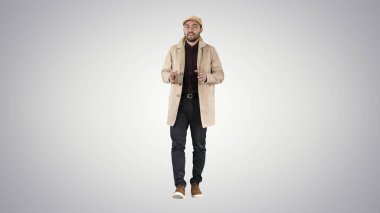 Trençkotlu genç adam kamerayla konuşuyor.