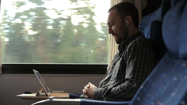Casual businessman in train with tablet and headphones watching video and smiling. — Stock Photo, Image