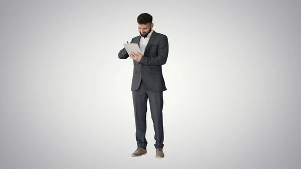 Uomo d'affari in piedi e utilizzando computer tablet su dorso gradiente — Foto Stock
