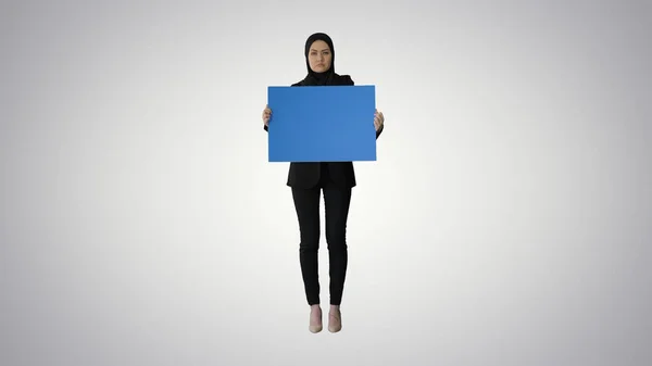 Mujer árabe seria en hijab sosteniendo cartel azul en blanco y mirando — Foto de Stock