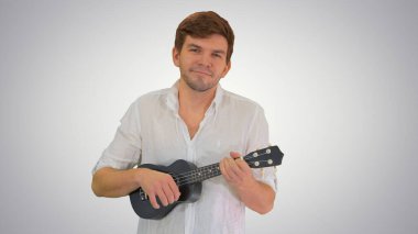 Ukulele çalan gülümseyen genç adam kameraya bakıyor.