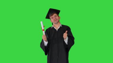 Mezuniyet cüppeli mutlu erkek öğrenci diplomasıyla poz veriyor ve Yeşil Ekran, Chroma Key 'de baş parmak gösteriyor..