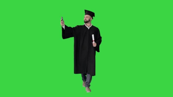 Homme portant le peignoir de fin d'études marchant et prenant selfie avec diplôme sur un écran vert, Chroma Key. — Video