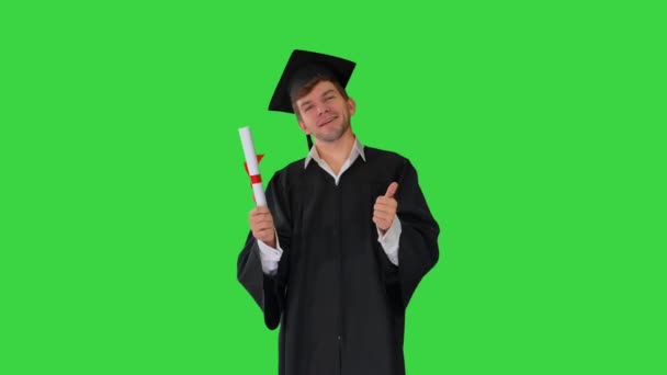 Feliz estudiante masculino en bata de graduación posando con su diploma y mostrando los pulgares hacia arriba en una pantalla verde, Chroma Key. — Vídeo de stock