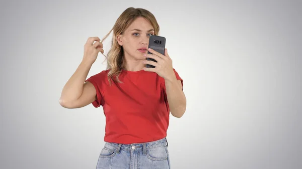Гарна молода жінка вирівнює волосся, дивлячись на мобільний — стокове фото