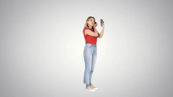 Mujer bastante joven aplicando rímel mirando su teléfono en grado —  Fotos de Stock