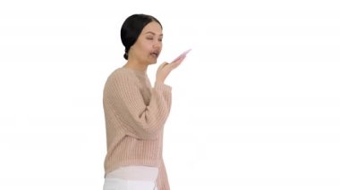 Genç bir kadın telefonda konuşuyor. Beyaz arka planda yürürken yüzüne doğru tutuyor..