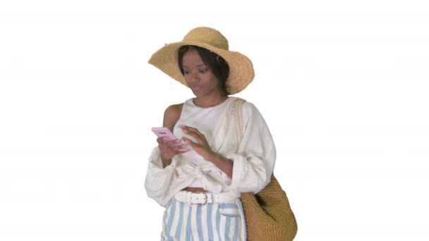 Χαμογελώντας νεαρή Αφροαμερικανή με ψάθινο καπέλο που στέλνει μηνύματα στο κινητό της σε λευκό φόντο. — Αρχείο Βίντεο