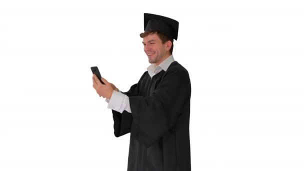 Sonriente estudiante masculino en vestido de graduación que muestra el campus a través de videollamada en su teléfono en fondo blanco. — Vídeos de Stock